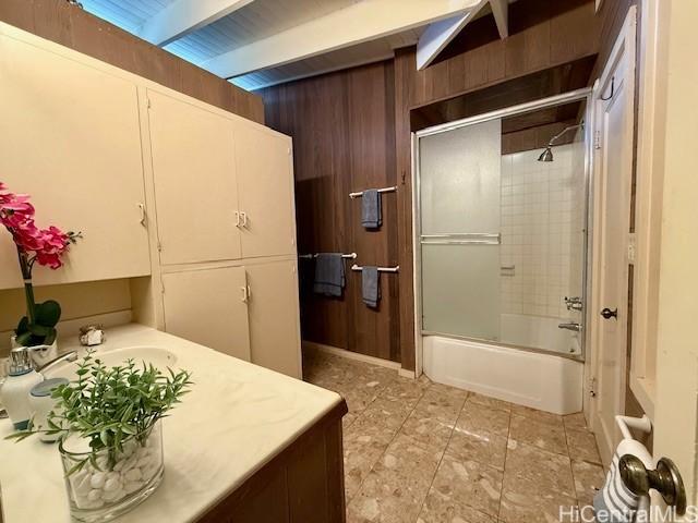 bathroom featuring wooden walls, bath / shower combo with glass door, and beam ceiling