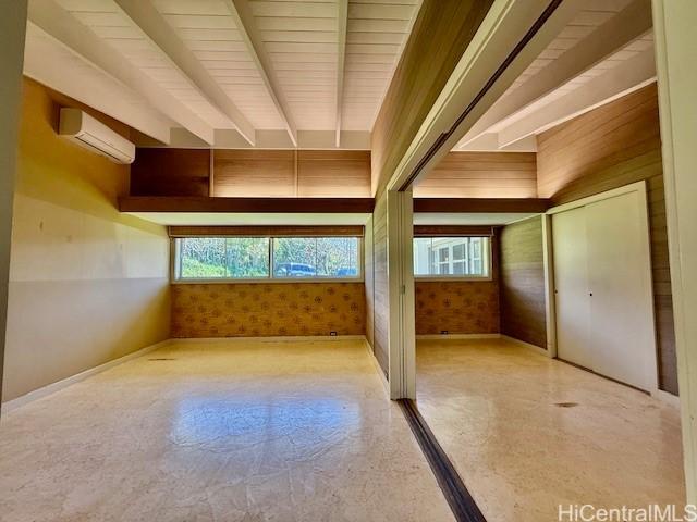 unfurnished room featuring beamed ceiling and a wall unit AC