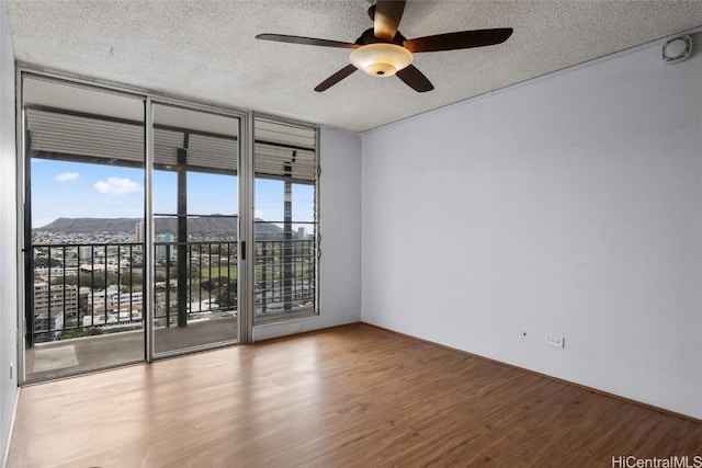 unfurnished room with a wall of windows, a mountain view, hardwood / wood-style floors, and a textured ceiling