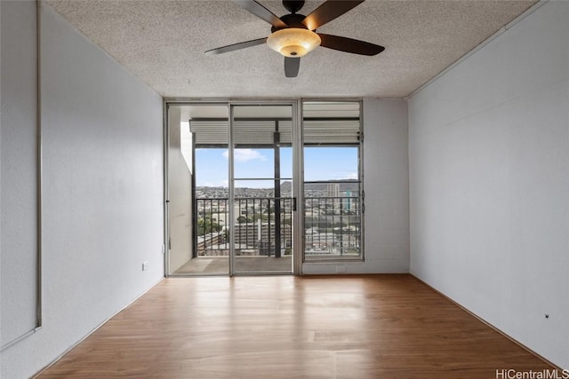 spare room with expansive windows, ceiling fan, light hardwood / wood-style floors, and a textured ceiling