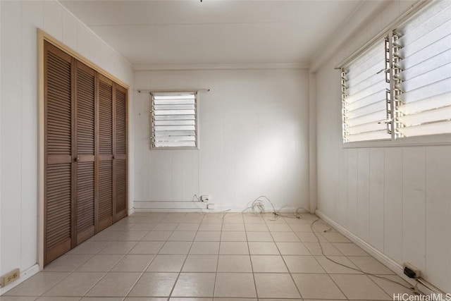 unfurnished bedroom with multiple windows, light tile patterned flooring, crown molding, and a closet