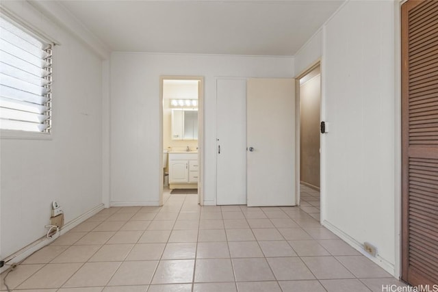 unfurnished bedroom with sink, light tile patterned floors, crown molding, ensuite bath, and a closet