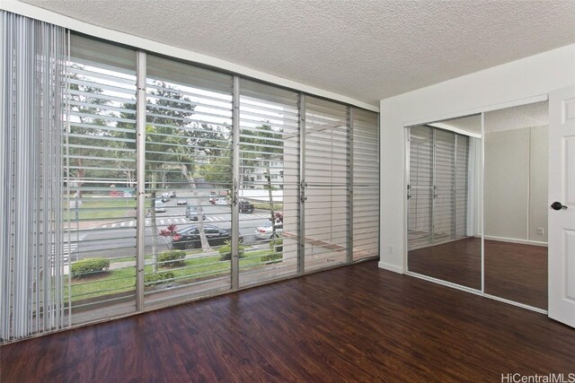 unfurnished bedroom with expansive windows, dark wood-type flooring, a textured ceiling, and a closet