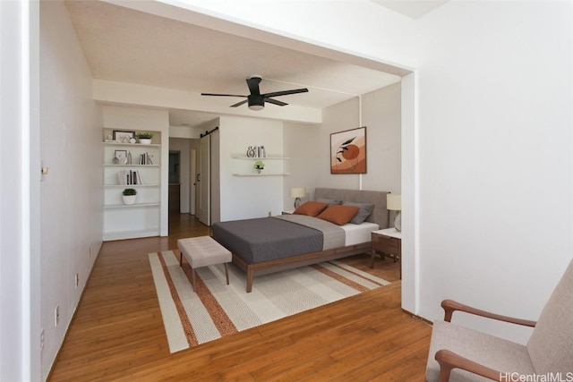 bedroom with ceiling fan, wood-type flooring, and a barn door