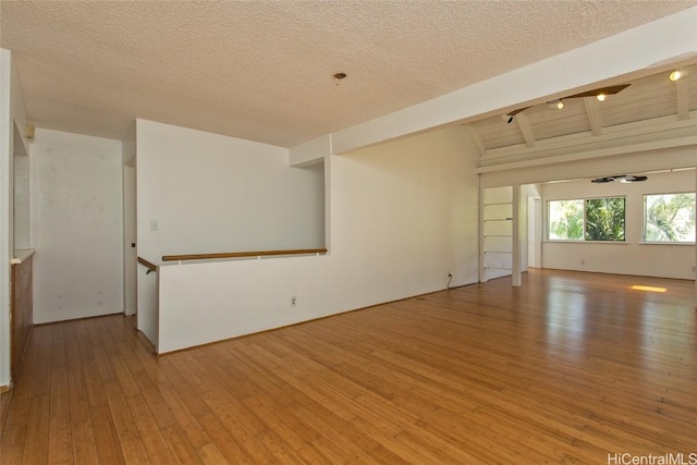 empty room featuring hardwood / wood-style flooring, vaulted ceiling with beams, and a textured ceiling