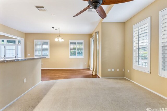 unfurnished living room with ceiling fan with notable chandelier and light carpet