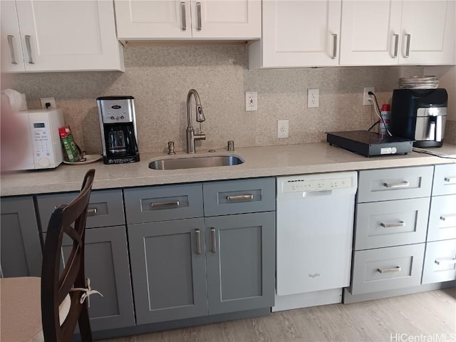 kitchen with white cabinets, white dishwasher, gray cabinets, light countertops, and a sink