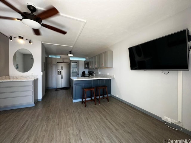 kitchen featuring gray cabinetry, stainless steel fridge, dark hardwood / wood-style flooring, a kitchen breakfast bar, and kitchen peninsula