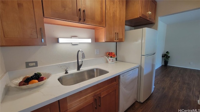 kitchen with white appliances, brown cabinetry, dark wood-style flooring, light stone countertops, and a sink