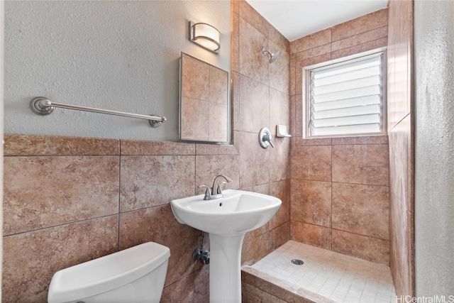 full bathroom featuring toilet, tiled shower, and tile walls