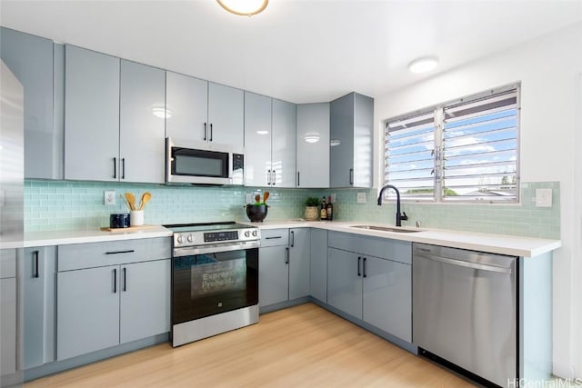 kitchen with tasteful backsplash, light countertops, appliances with stainless steel finishes, light wood-style floors, and a sink