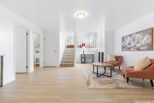 sitting room with light wood-type flooring, stairs, and baseboards