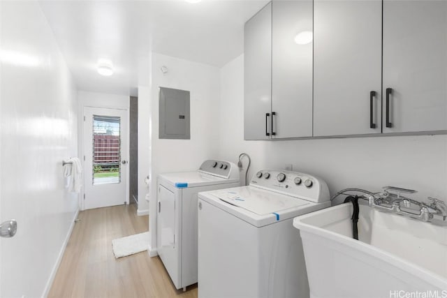 clothes washing area with cabinet space, electric panel, washer and dryer, light wood-style floors, and a sink