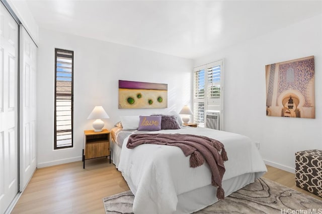 bedroom with cooling unit, a closet, baseboards, and light wood finished floors