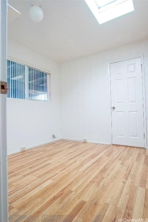 empty room featuring a skylight and light wood-type flooring