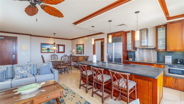 kitchen featuring stainless steel appliances, a center island with sink, wall chimney range hood, and hanging light fixtures