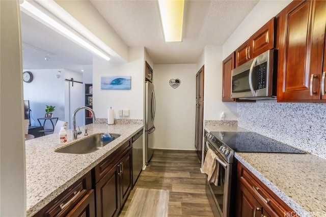 kitchen featuring sink, dark wood-type flooring, stainless steel appliances, light stone countertops, and a barn door