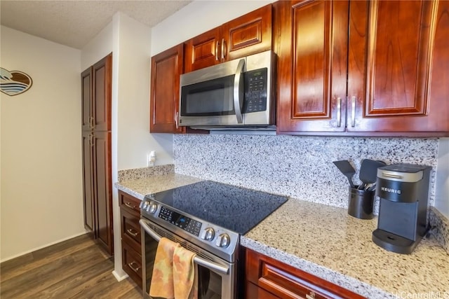 kitchen featuring dark wood-type flooring, appliances with stainless steel finishes, light stone countertops, and backsplash