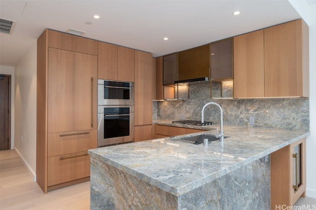 kitchen with light stone counters, sink, tasteful backsplash, and kitchen peninsula