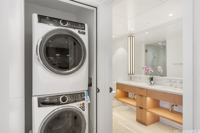 clothes washing area with stacked washer and dryer, sink, and light wood-type flooring