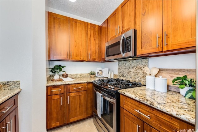 kitchen featuring stainless steel appliances, tasteful backsplash, a textured ceiling, and light stone counters