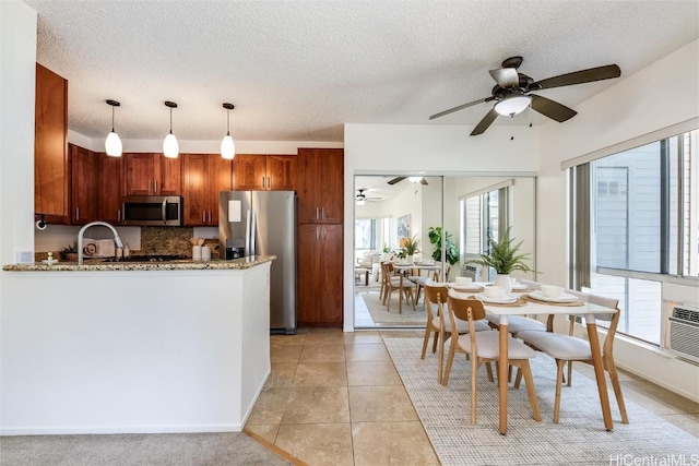 kitchen featuring decorative light fixtures, light tile patterned floors, appliances with stainless steel finishes, kitchen peninsula, and light stone countertops