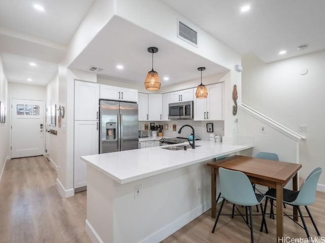 kitchen featuring white cabinetry, sink, kitchen peninsula, stainless steel appliances, and light hardwood / wood-style flooring