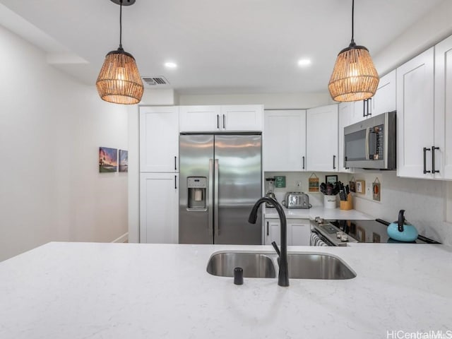 kitchen with sink, white cabinets, hanging light fixtures, stainless steel appliances, and light stone countertops