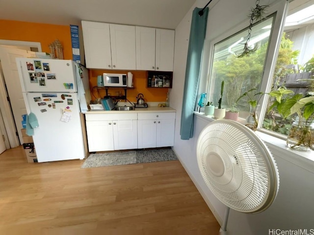 kitchen with white appliances, light hardwood / wood-style flooring, and white cabinets