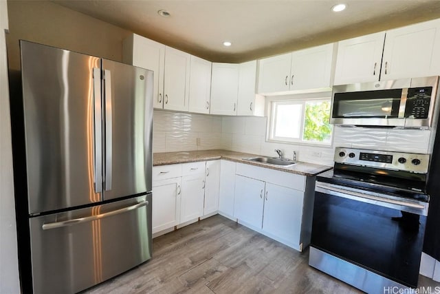 kitchen with sink, appliances with stainless steel finishes, white cabinetry, light hardwood / wood-style floors, and decorative backsplash