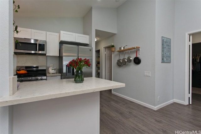 kitchen featuring stainless steel appliances, dark hardwood / wood-style flooring, kitchen peninsula, and white cabinets