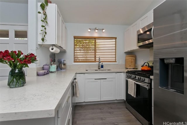 kitchen featuring appliances with stainless steel finishes, sink, white cabinets, light stone counters, and dark wood-type flooring