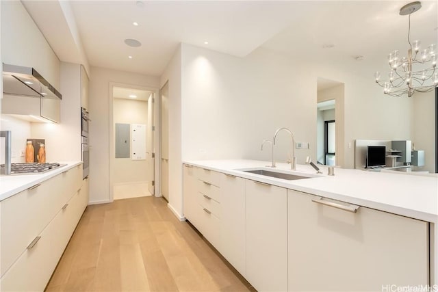 kitchen with decorative light fixtures, sink, white cabinets, wall chimney range hood, and light hardwood / wood-style flooring