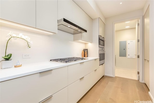 kitchen with wall chimney exhaust hood, electric panel, stainless steel appliances, light hardwood / wood-style floors, and white cabinets