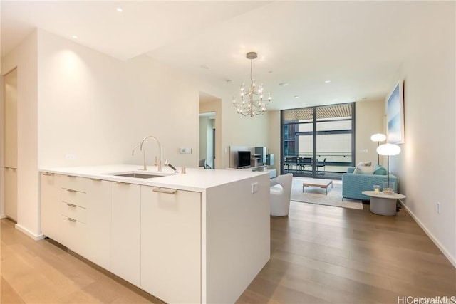 kitchen featuring pendant lighting, sink, white cabinetry, a chandelier, and light wood-type flooring