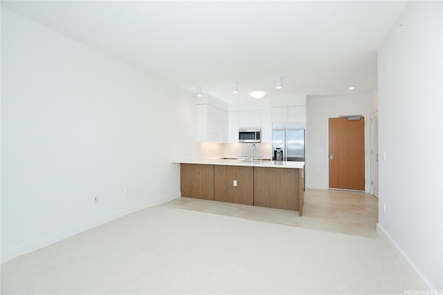 kitchen featuring white cabinets, stainless steel appliances, a peninsula, modern cabinets, and light countertops