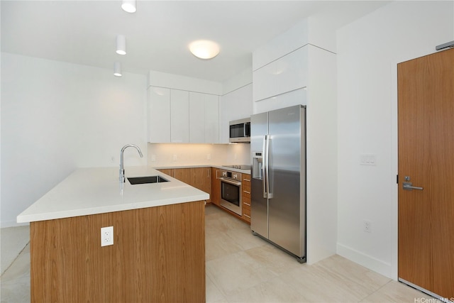 kitchen with white cabinets, a peninsula, a sink, light countertops, and appliances with stainless steel finishes