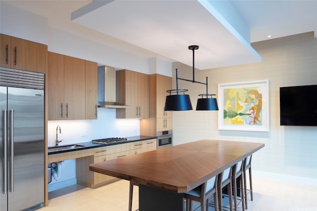kitchen featuring wall chimney range hood, dark countertops, a sink, stainless steel appliances, and decorative light fixtures
