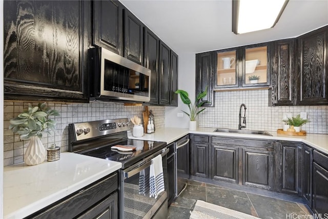 kitchen featuring a sink, light countertops, glass insert cabinets, appliances with stainless steel finishes, and backsplash