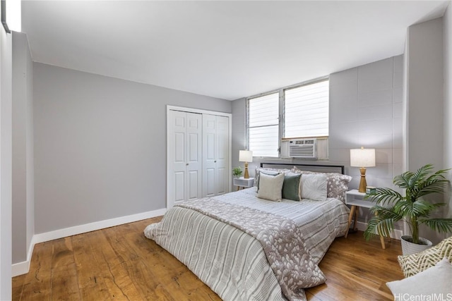 bedroom with hardwood / wood-style floors, cooling unit, baseboards, and a closet