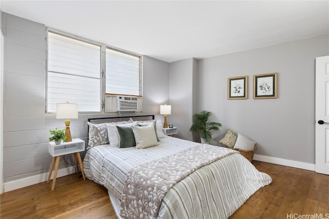 bedroom with cooling unit, baseboards, and wood finished floors