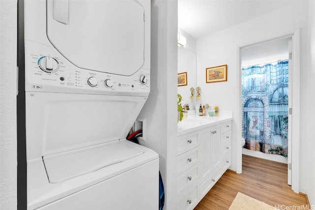 laundry area featuring stacked washer / drying machine, light hardwood / wood-style flooring, and sink