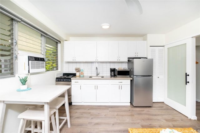 kitchen with a breakfast bar, sink, white cabinets, stainless steel appliances, and light hardwood / wood-style flooring