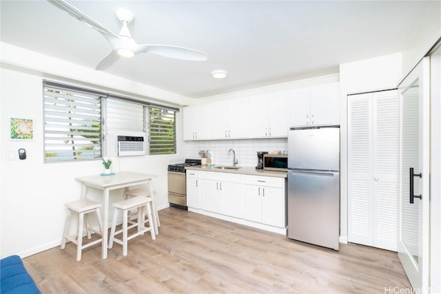 kitchen with appliances with stainless steel finishes, sink, backsplash, white cabinets, and light wood-type flooring