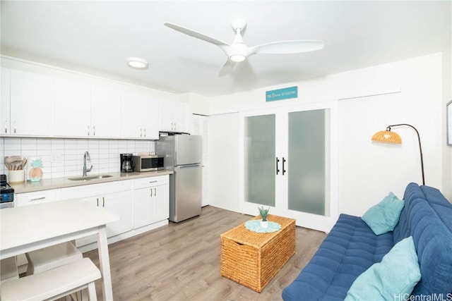 kitchen featuring tasteful backsplash, white cabinetry, sink, stainless steel appliances, and light wood-type flooring