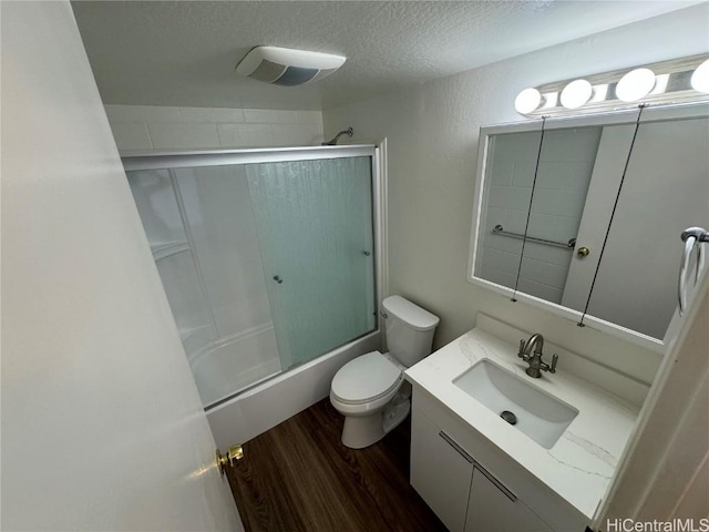 full bathroom with hardwood / wood-style flooring, combined bath / shower with glass door, vanity, a textured ceiling, and toilet