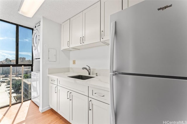 kitchen featuring refrigerator, stacked washer / dryer, sink, white cabinets, and expansive windows