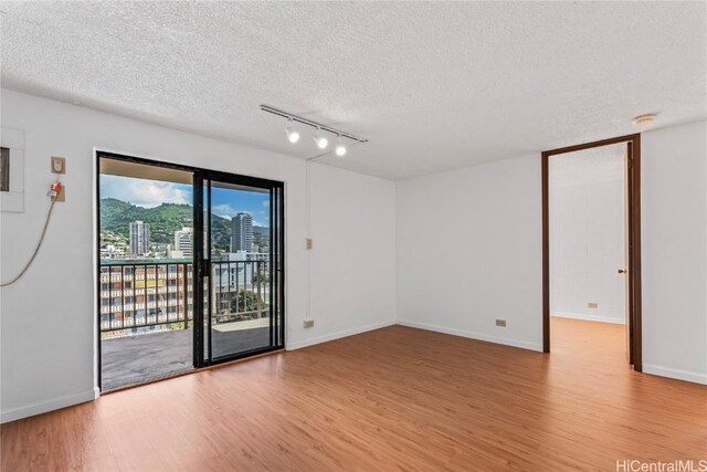 spare room featuring rail lighting, light hardwood / wood-style flooring, and a textured ceiling