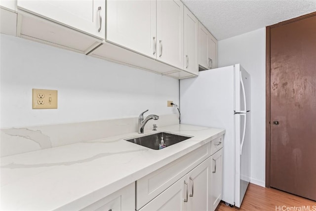 kitchen with light stone counters, light wood-style floors, white cabinets, a textured ceiling, and a sink