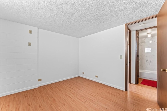 unfurnished room featuring baseboards, light wood-type flooring, and a textured ceiling